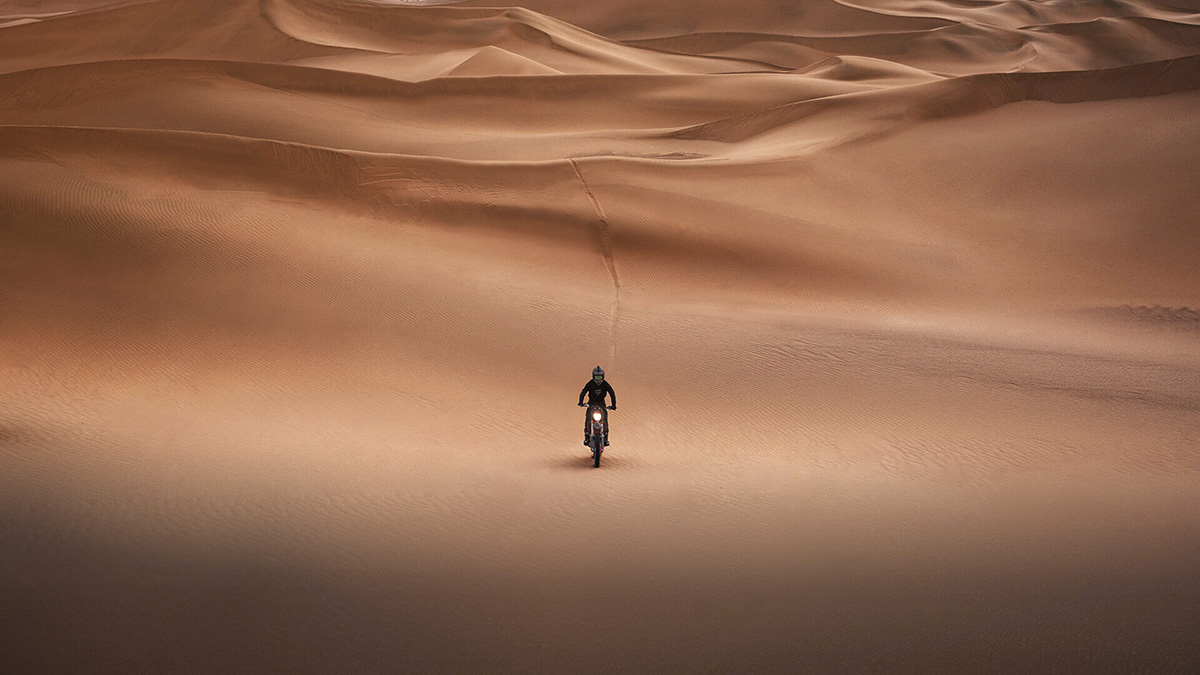 広大な砂漠の真ん中をオフロードバイクが走るのを正面から捉えた写真